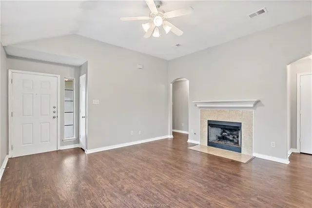 an empty room with wooden floor fireplace cabinet and windows
