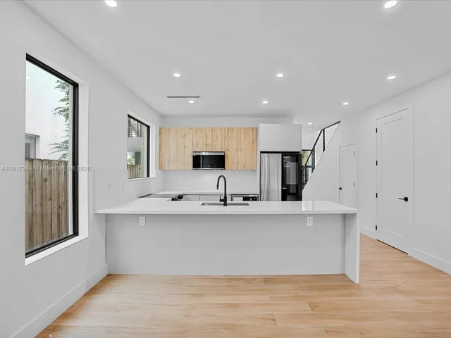 a view of kitchen with stainless steel appliances sink large window and wooden floor