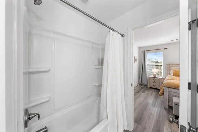 a view of a white house in front of a big yard with plants and large tree