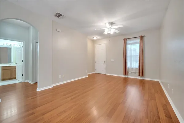a view of an empty room with wooden floor and a ceiling fan