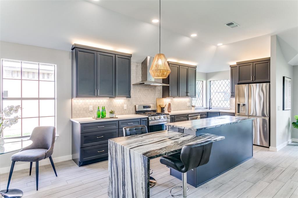 3913 Bobbin Lane Addison, TX 75001 - Photo 7 of 23 Kitchen featuring stainless steel appliances, a kitchen bar, a center island, dark stone counters, and light wood-style floors