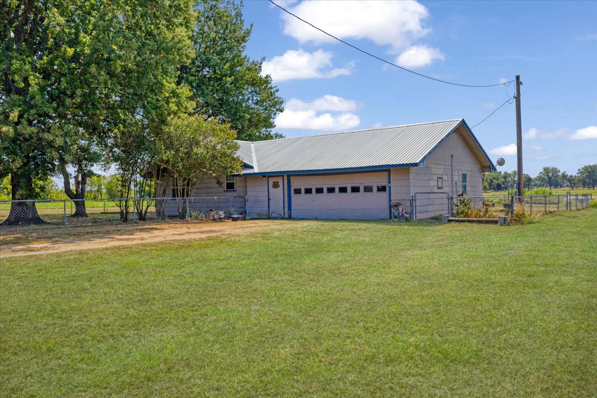 4840 River Road Colbert, OK 74733 - Photo 18 of 19 Attached garage with multiple bays, corrugated metal roofing, and a chain-link fence perimeter