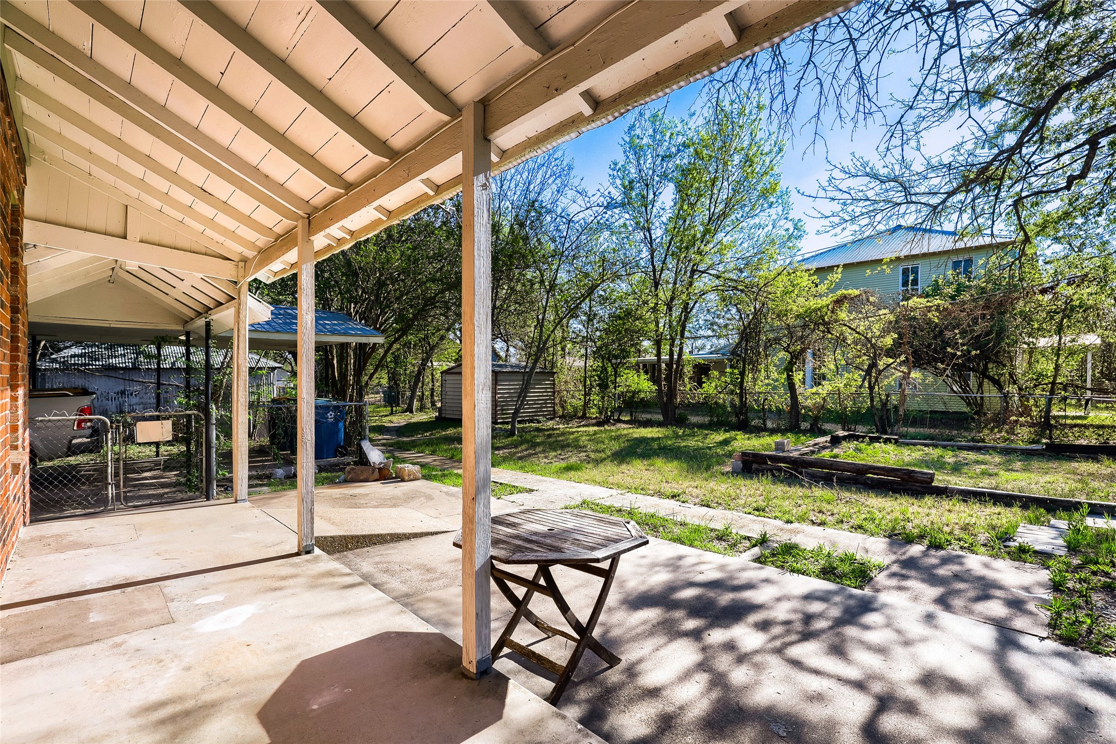 208 North Ave B Elgin, TX 78621 - Photo 26 of 29 This photo showcases a spacious backyard with a covered patio, perfect for outdoor relaxation or entertaining. The area is shaded with mature trees, offering a serene and private atmosphere.