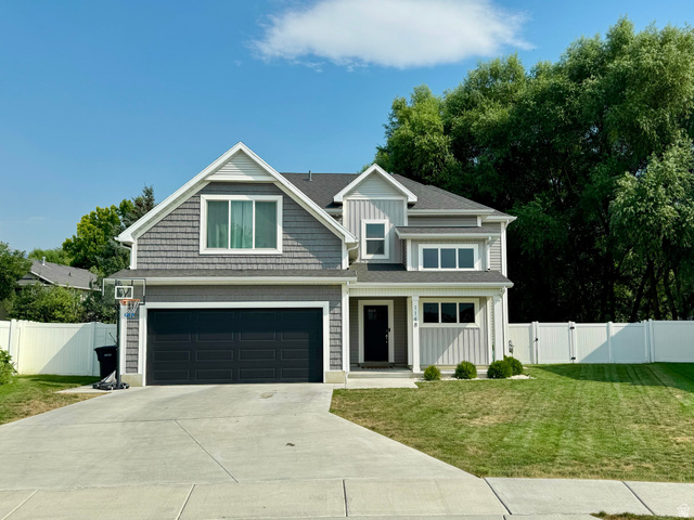 1148 290 South Logan, UT 84321 - Photo 1 of 34 Two-story exterior with a gray and white facade, featuring a dark garage door, a concrete driveway, a front entry with a small porch, and a white fence