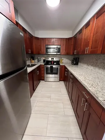 a large kitchen with stainless steel appliances granite countertop a stove a sink dishwasher and a refrigerator with wooden cabinets