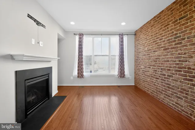 a view of an empty room with wooden floor fireplace and a window
