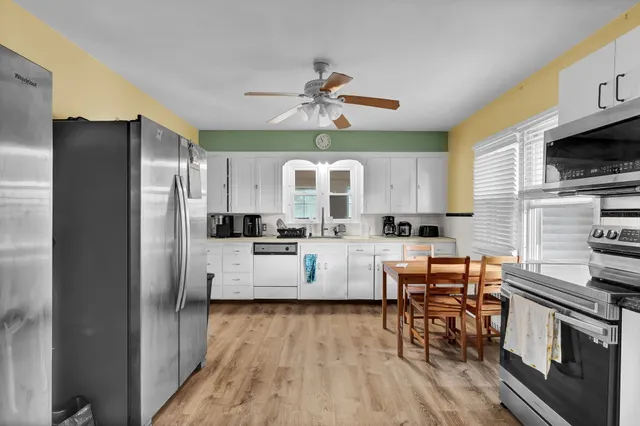 a kitchen with stainless steel appliances a refrigerator a stove top oven a sink dishwasher and white cabinets with wooden floor