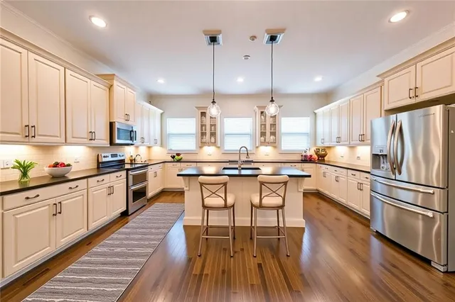 a kitchen with stainless steel appliances kitchen island granite countertop a stove a sink a refrigerator and white cabinets with wooden floor