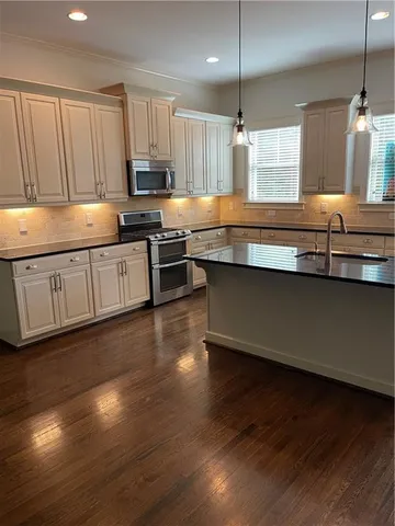a kitchen with stainless steel appliances granite countertop a sink dishwasher a stove a refrigerator and a microwave oven on the wooden floor