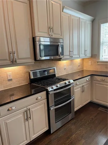 a white kitchen with granite countertop a stove a sink and a microwave
