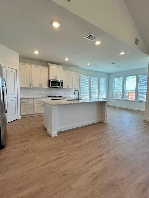 1833 Welsh Road Celina, TX 75009 - Photo 1 of 8 Open-concept kitchen featuring white cabinetry, stainless steel appliances, a central island with an undermount sink, recessed lighting, and wood-finish flooring extending into the adjacent living space