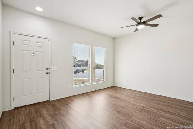 an empty room with wooden floor fan and windows