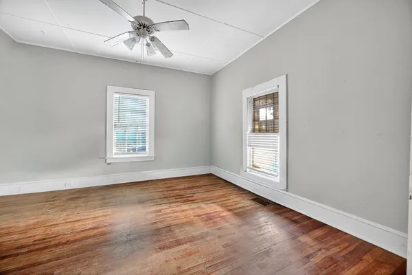 an empty room with wooden floor chandelier fan and windows