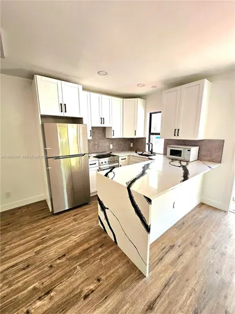 a kitchen with stainless steel appliances granite countertop a refrigerator a stove a sink and white cabinets with wooden floor