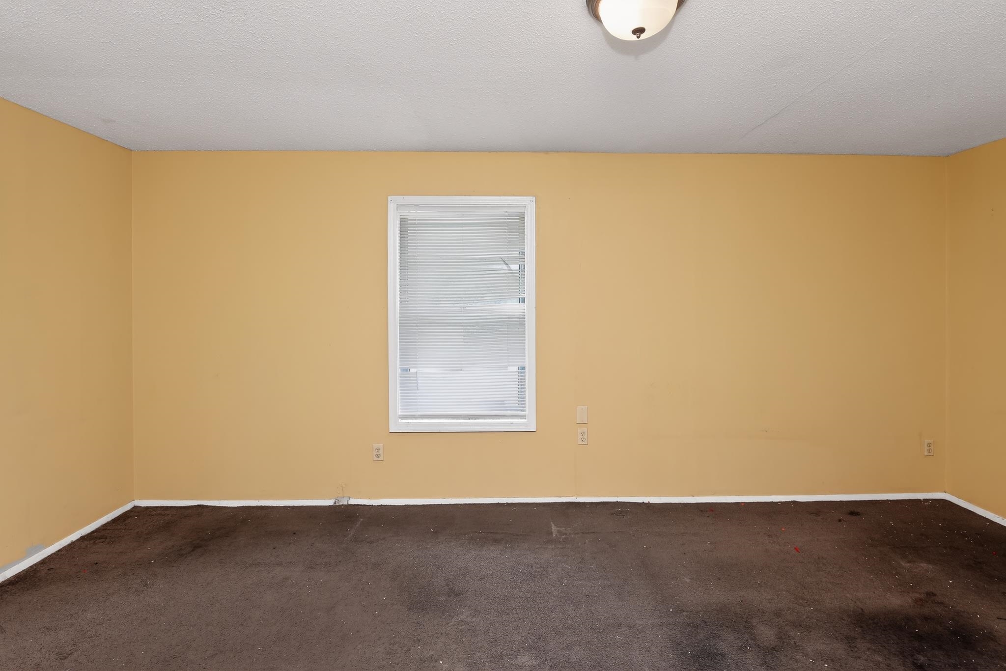 645 Parkrose Road Memphis, TN 38109 - Photo 28 of 32 Room featuring warm yellow walls, a single window with white blinds, dark carpeting, and a ceiling-mounted light fixture
