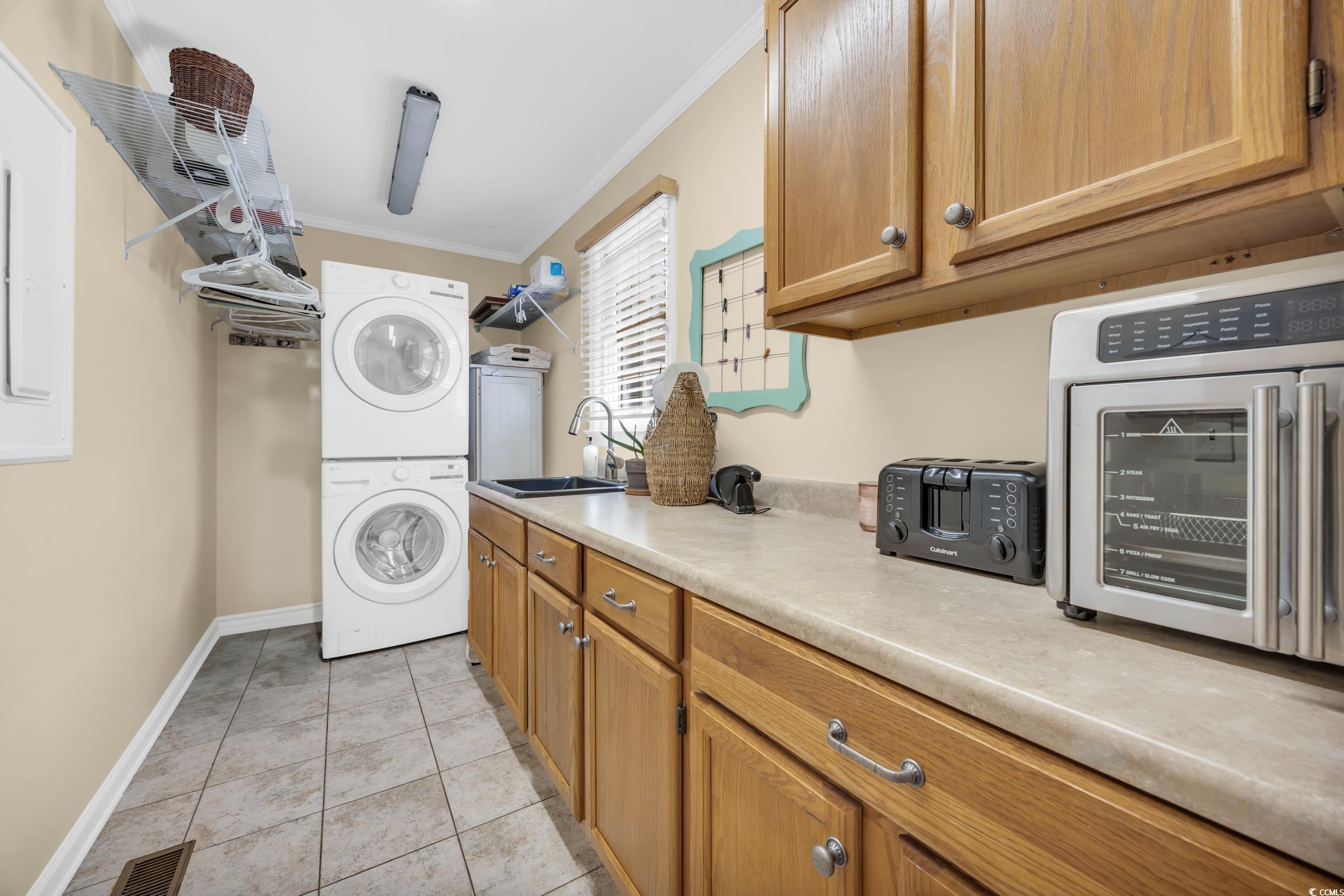 855 Riven Oak Drive Murrells Inlet, SC 29576 - Photo 24 of 37 Laundry room featuring ornamental molding, stacked washer / drying machine, light tile patterned floors, and cabinet space