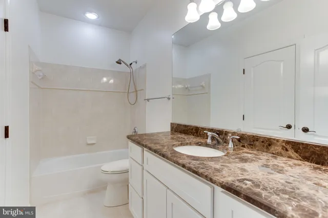 a bathroom with a granite countertop sink a toilet a mirror and shower