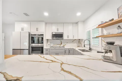 a kitchen with stainless steel appliances kitchen island granite countertop a sink a stove a refrigerator with white cabinets and wooden floor