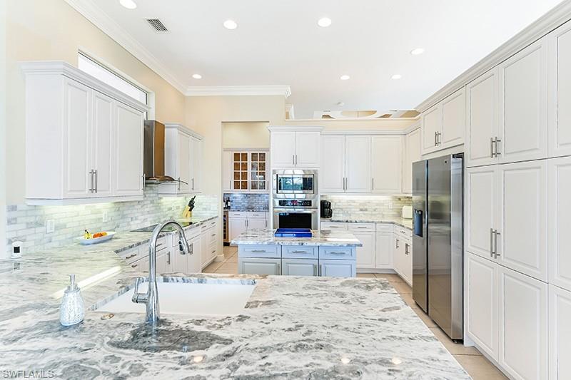 11234 5 Oaks Lane Naples, FL 34120 - Photo 9 of 34 a kitchen with stainless steel appliances kitchen island granite countertop a refrigerator and cabinets