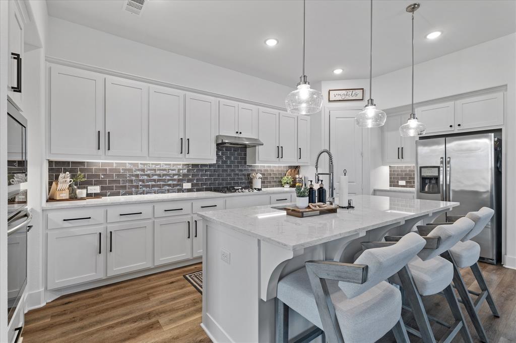1332 Thompson Road Argyle, TX 76226 - Photo 8 of 36 Kitchen featuring stainless steel appliances, light stone counters, white cabinets, a kitchen island with sink, and dark wood finished floors