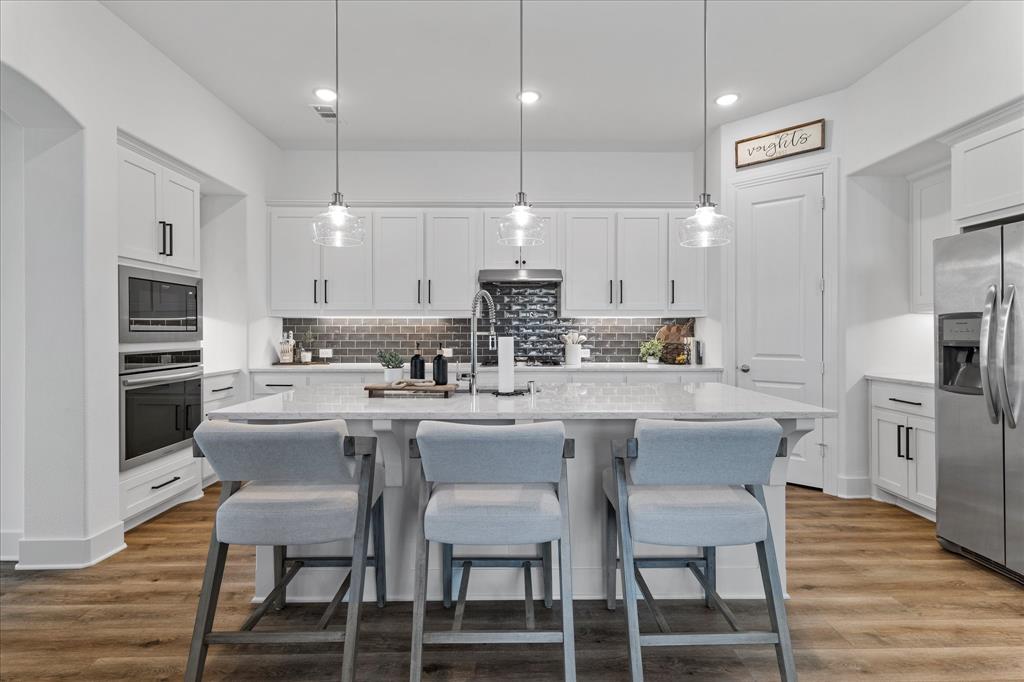 1332 Thompson Road Argyle, TX 76226 - Photo 9 of 36 Kitchen with a breakfast bar, a kitchen island with sink, stainless steel appliances, decorative light fixtures, and white cabinetry