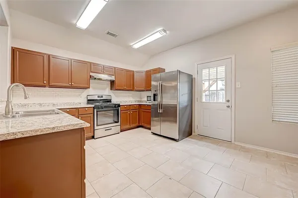 a kitchen with stainless steel appliances a sink a stove a refrigerator cabinets and a window