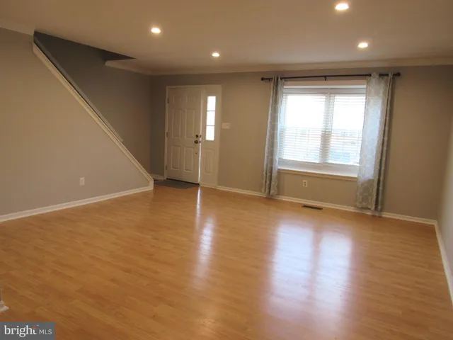 an empty room with wooden floor and windows with curtains
