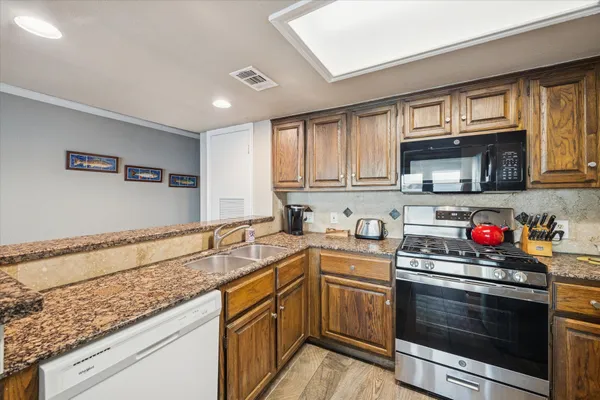 a kitchen with granite countertop a sink dishwasher stove and microwave with wooden cabinets