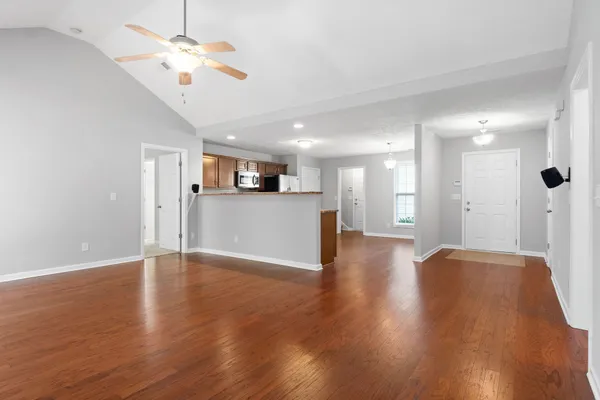 a view of an empty room with wooden floor and a kitchen
