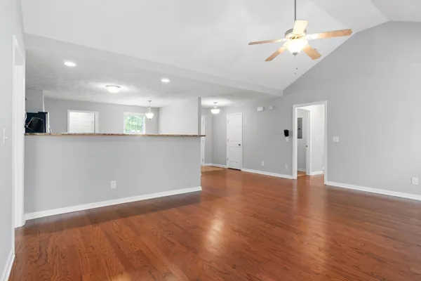 a view of an empty room with wooden floor and a ceiling fan