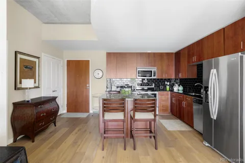 a kitchen with stainless steel appliances a refrigerator a stove a sink a dining table and chairs with wooden floor