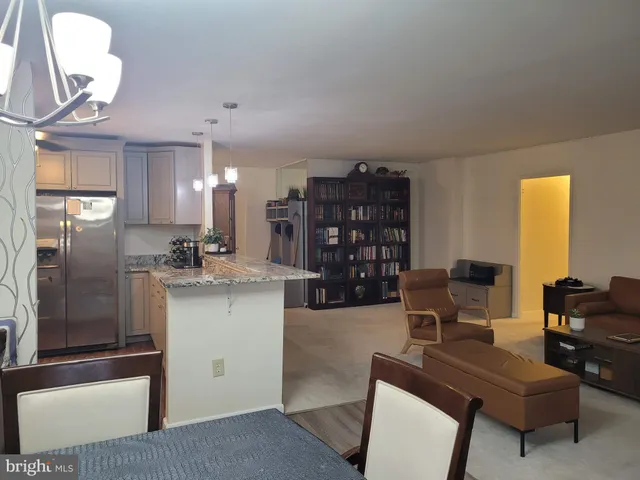 a kitchen with stainless steel appliances kitchen island granite countertop a refrigerator a stove a dining table and chairs with wooden floor