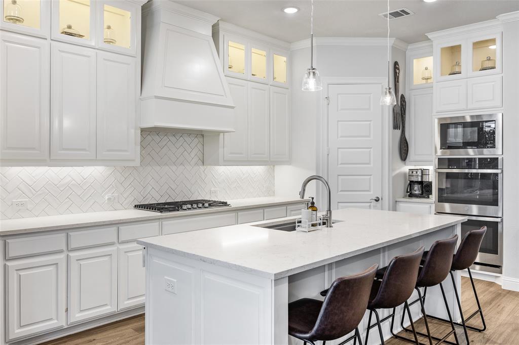 2628 Flycatcher Road Fort Worth, TX 76118 - Photo 12 of 38 Kitchen featuring light stone counters, light wood finished floors, backsplash, a kitchen island with sink, and white cabinets
