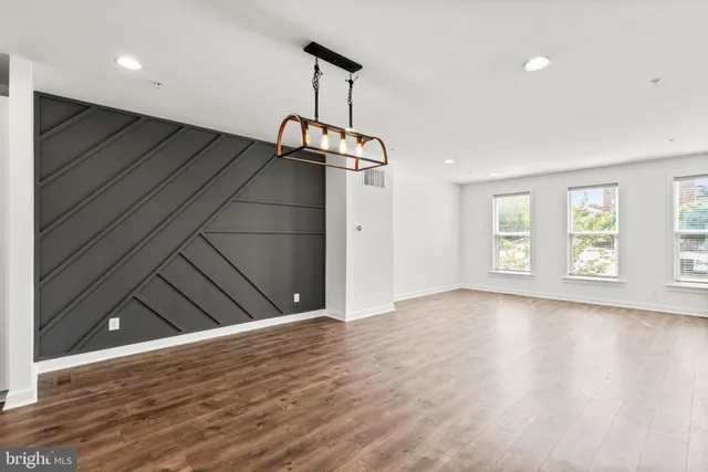 a view of an empty room with wooden floor fridge and a window