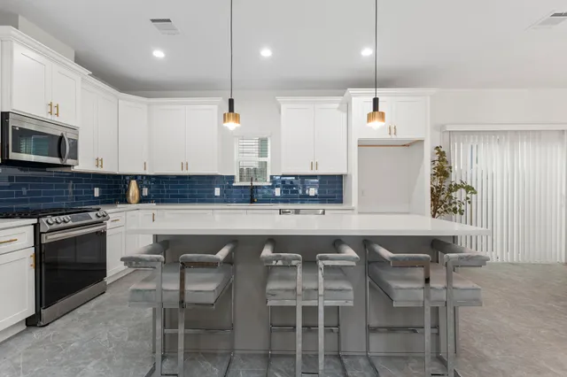 a kitchen with stainless steel appliances a sink a stove a center island and chairs