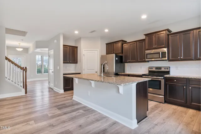 a large kitchen with stainless steel appliances granite countertop a stove top oven a sink and dishwasher a refrigerator with wooden floor