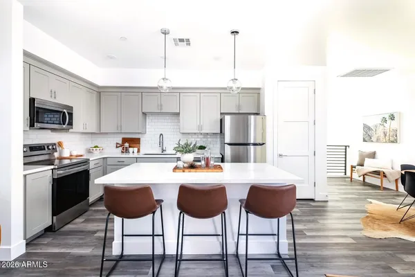 a kitchen with stainless steel appliances kitchen island granite countertop a dining table chairs and a refrigerator