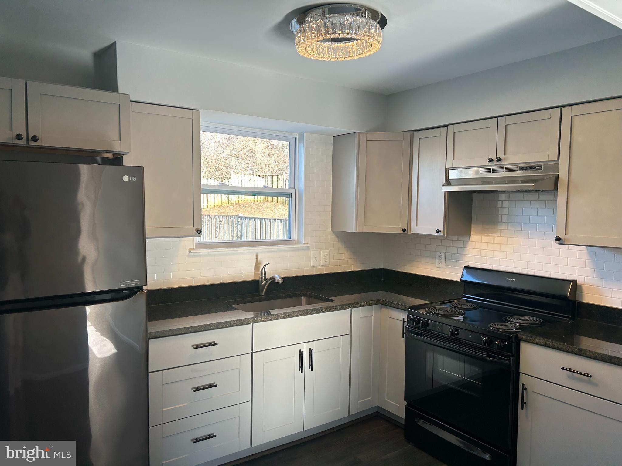 a kitchen with granite countertop a refrigerator a sink and white cabinets