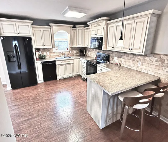a kitchen with granite countertop a refrigerator a stove a sink dishwasher and white cabinets with wooden floor