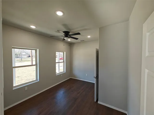 an empty room with wooden floor fan and windows
