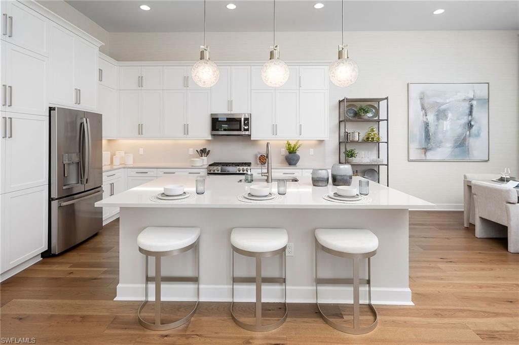 2695 Ridgecrest Place Naples, FL 34112 - Photo 2 of 13 Kitchen with stainless steel appliances, light countertops, a kitchen breakfast bar, white cabinets, and light wood-style flooring