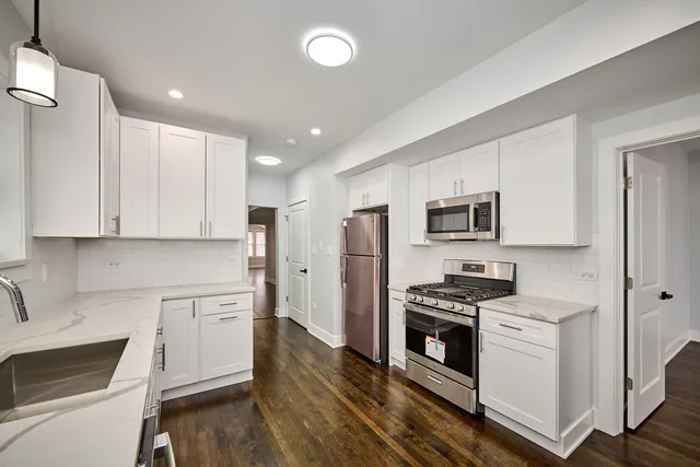 a kitchen with stainless steel appliances a stove top oven a sink a refrigerator white cabinets and wooden floor