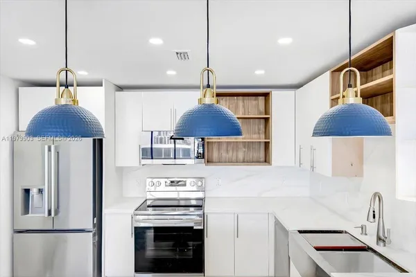 a kitchen with stainless steel appliances a stove a refrigerator a sink a counter space and a couch