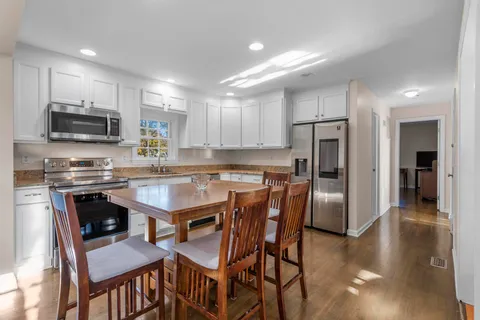 a kitchen with stainless steel appliances granite countertop a dining table chairs refrigerator and microwave
