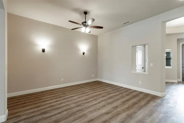 a view of an empty room with wooden floor and a ceiling fan