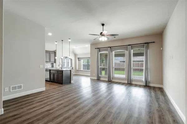 a view of an empty room with wooden floor and a kitchen