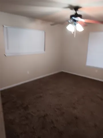 an empty room with a chandelier fan and windows