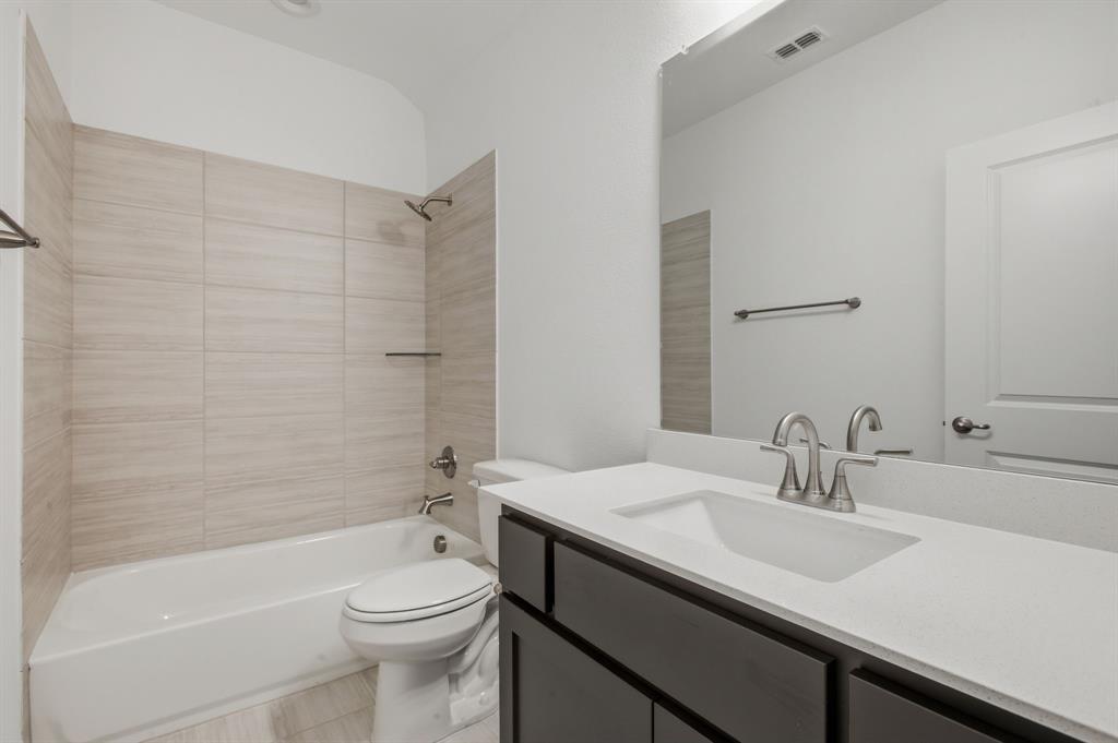 2911 Hanscom Street Forney, TX 75126 - Photo 40 of 40 Bathroom featuring a white bathtub, light-toned tile surround, and a dark wood-finish vanity with an integrated sink and light-toned countertop