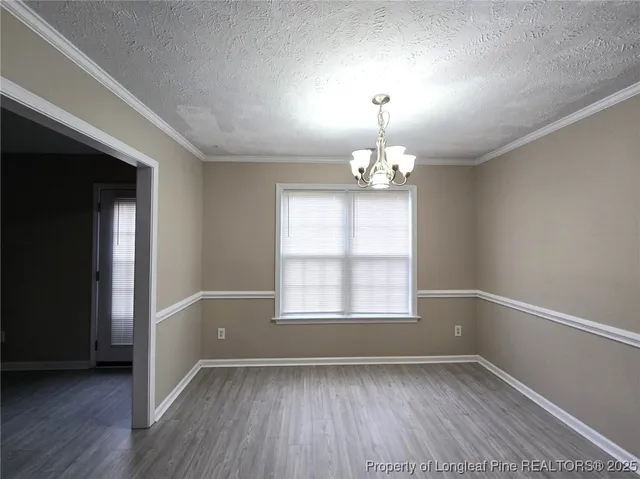 an empty room with wooden floor chandelier and windows