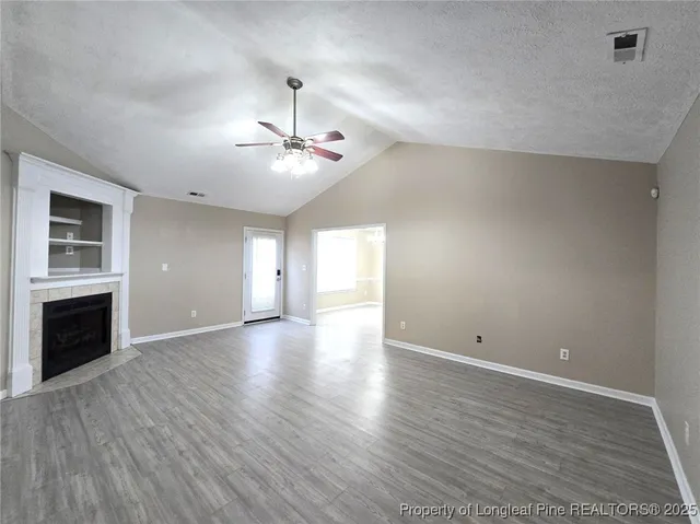 an empty room with wooden floor fireplace and windows